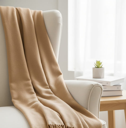 Beige blanket draped over a white chair in a bright room with a small table and plant.