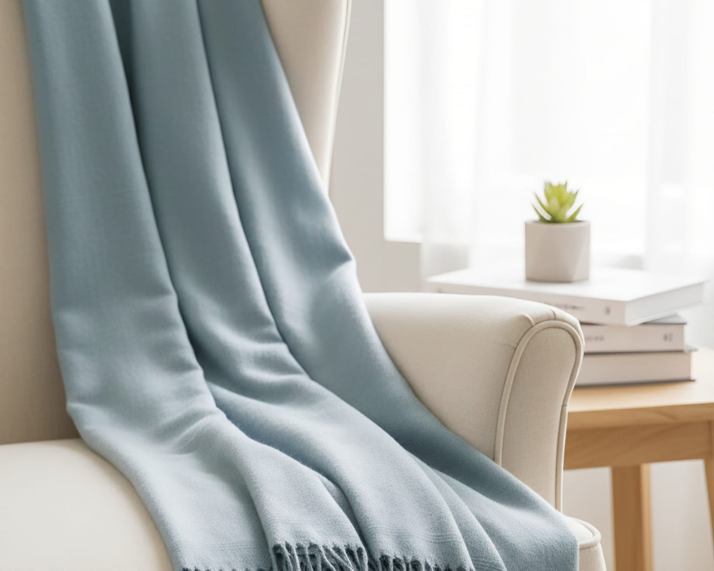 Light blue throw blanket draped over a beige armchair in a bright room with a small table and plant.
